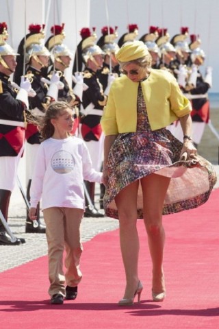A bela Rainha Máxima da Holanda anda de mãos dadas no tapete vermelho com sua filha e é surpreendida pelo vento forte que levanta seu vestido estampado deixando a mostra um bonito par de pernas!