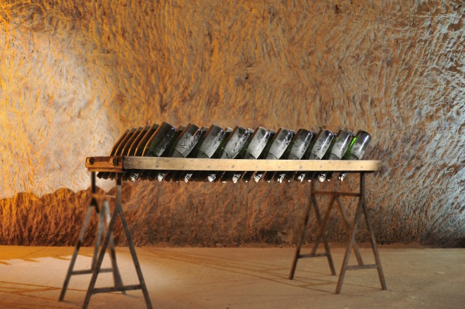 Imagem de um adega sub-terrânea , que eram túneis construídos pelos romanos, onde temos várias garrafas apoiadas de ponta cabeça, numa mesa de descanso , com pouca iluminação e temperatura controlada.