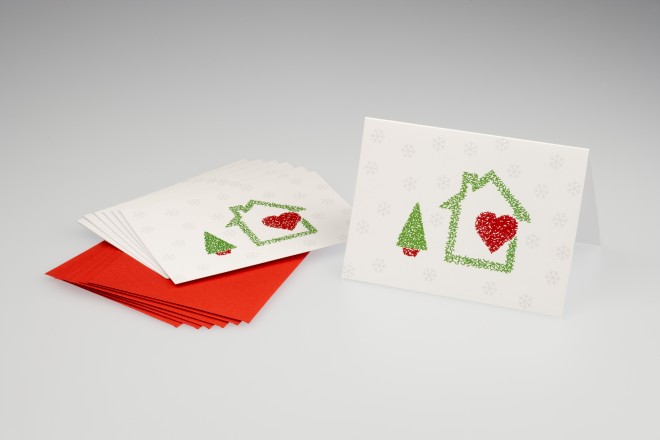 Cartão de Natal, na cor cinza, tendo ao centro um envelope vermelho e sobre ele um cartão com um desenho de uma casinha com um coração vermelho dentro dela e ao lado uma pequena arvore verde com caule na cor vermelha.