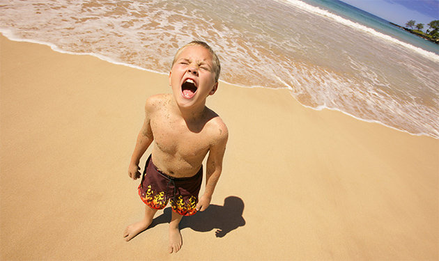 foto mostra um menino de aproximadamente 8 anos gritando de costas para o mar