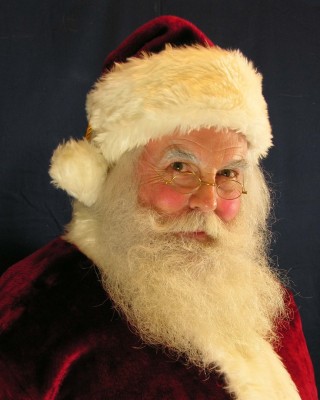 Imagem do rosto do Papai Noel, velho senhor com faces rosadas, grande barba branca, óculos e um gorro vermelho com a faixa branca de algodão.