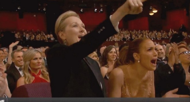 Imagem do auditório da entrega do Prêmio Oscar 2015. Em primeiro plano estão Maryl Streep e Jennifer Lopez, atrizes, aplaudindo efusivamente.
