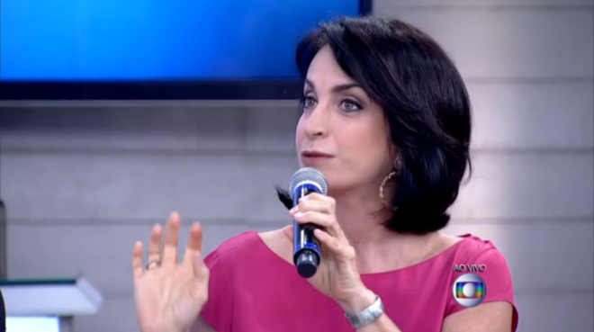Claudia Matarazzo, durante o programa Encontro com Fatima Bernardes da Rede Globo, ela está usando um vestido rosa, num close fechado, ela olha para a apresentadora, e segura um microfone com a mão esquerda. No seu pulso um relógio com pulseira prateada. 