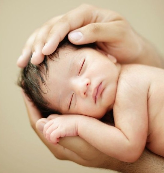 a foto mostra um recém nascido sendo segurado entre mãos do pai.