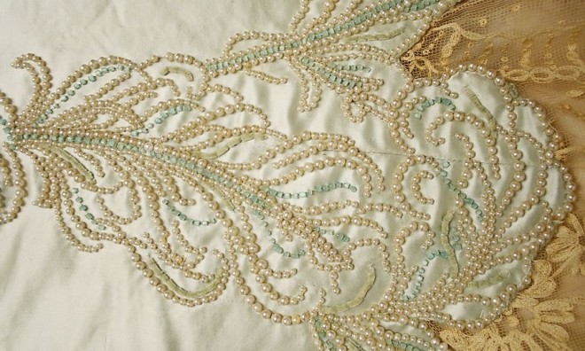 Bordado foto - tecido de cetim de seda creme ricamente bordado com pequenas pérolas e fios de ouro. Delicadas aplicações de renda em tom chá complementam o trabalho.