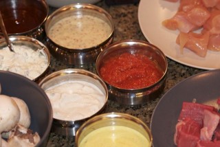 a foto mostra varios potinhos de inox com molhos. Mostarda, molho de iogurte, molho rose. Ao lado, dois potes com frango e carne.