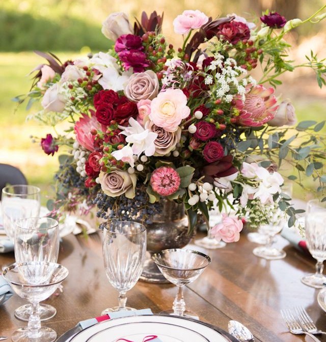 arranjo de flores em tons de rosas vermelhas e rosa, no centro de uma mesa de almoço toda montada.