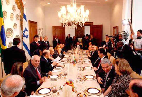 Almoço concedido ao Primeiro Ministro de Israel, Shimon Peres, na Ala Residencial do Palácio dos Bandeirantes em São Paulo, ele está sentado no centro da mesa ao lado do Governador. Outras 18 pessoas compõem a mesa. e muitos jornalistas filmam e fotografam a cena.