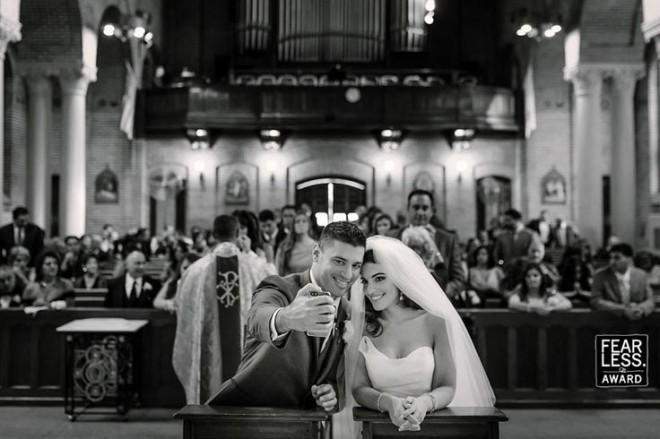 foto do interior de uma igreja em preto e branco, onde o noivo no altar, faz uma selfie com a noiva.