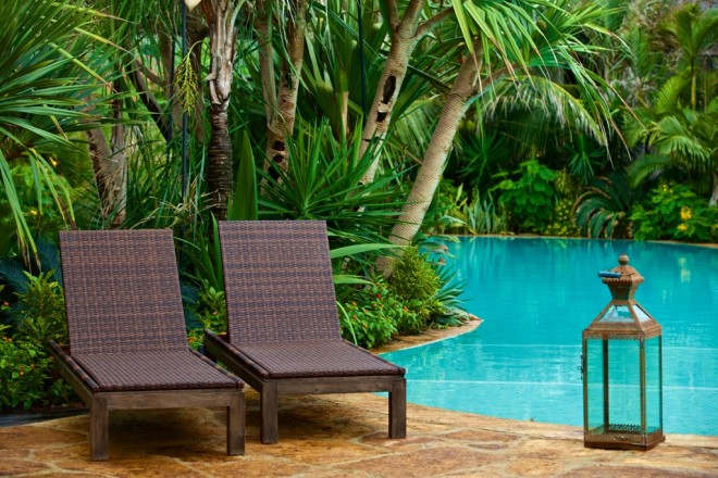 Detalhe da piscina do Hotel Lara, Aquiraz, Ceará, onde temos duas cadeiras de descanso, em madeira, ao fundo um lindo jardim com palmáceas.