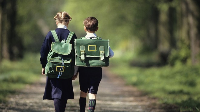 Boy (6-7) and girl (8-9) going  school through forest, rear view