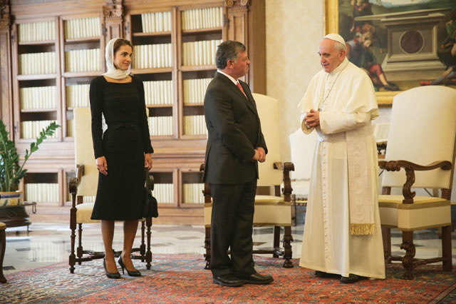 No salão de audiência do Vaticano, está de pé o Papa Francisco recebe o Rei Abdullah vestindo terno escuro e Rainha Rânia da Jordânia usando vestido preto, e véu rendado na cor creme. Sua Santidade veste sua tunica branca