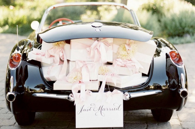 carro de luxo, visto de tras, com o porta-mala aberto e repleto de presentes . No para-choque uma placa "Just married".