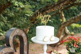 Uma mesa pequena e redonda apoia um prato de bolo branco com um cactus de açúcar verde confeitado enfeitando. Ao redor pequenos vasos de cactos naturais compõem o visual.