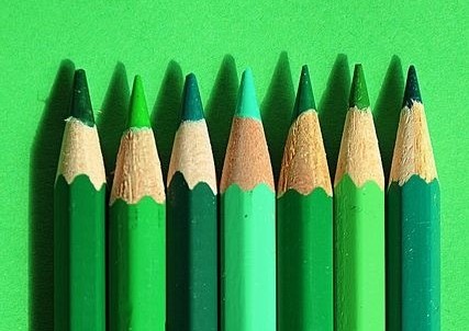 sete lápis em diferentes tons de verde estão enfileirados e apontados com suas pontas para cima sobre um fundo verde claro bem forte