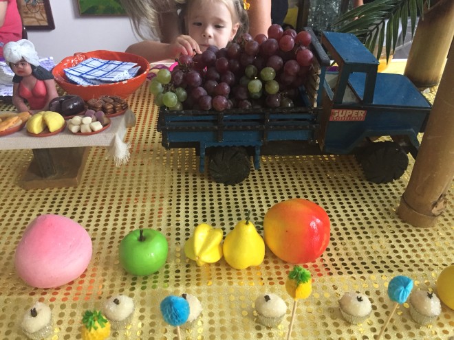 Mesa de festa, com mini caminhão, com uvas roxas e outras frutas fantasias decorando a mesa.