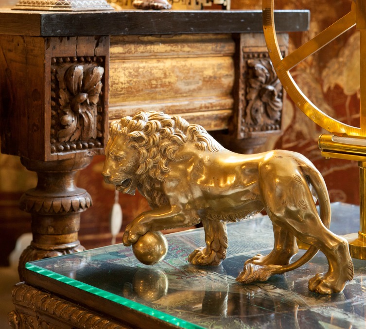Detalhe do artesanato com a imagem de um leão, dourado, sobre uma mesa de centro com base de vidro.