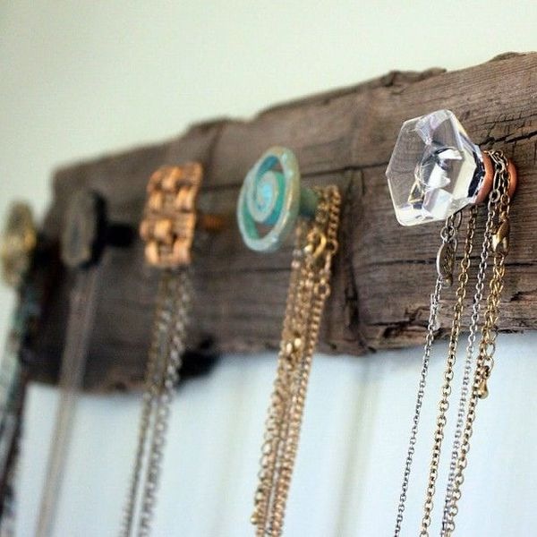 uma tábua rústica está pendurada na parede e nela, vários puxadores coloridos estão servindo de ganchos para colares e correntes de bijuteria