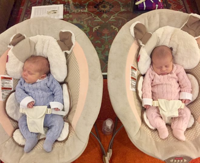 dois bebês com cerca de um mês estão em duas cestas diferentes um vestido de azul outro de cor de rosa e ambos dormem .