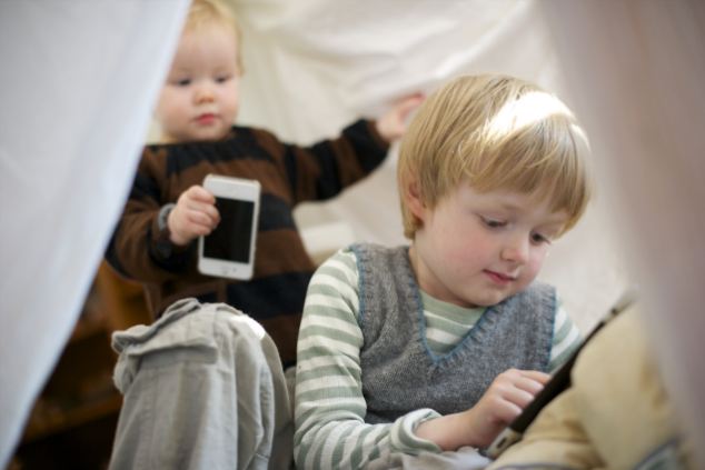 duas crianças uma mais velha do que a outra (5 anos) e (1 anos), que estão brincando um smartphones e tablets.