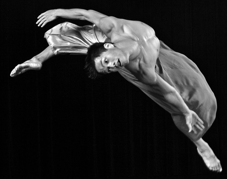 Bailarino caindo em uma pirueta com braços e pernas em movimento formando um arco em um retrato de grande impacto.A foto está em preto e branco e o jogo de sombras contribui para a beleza do conjunto.