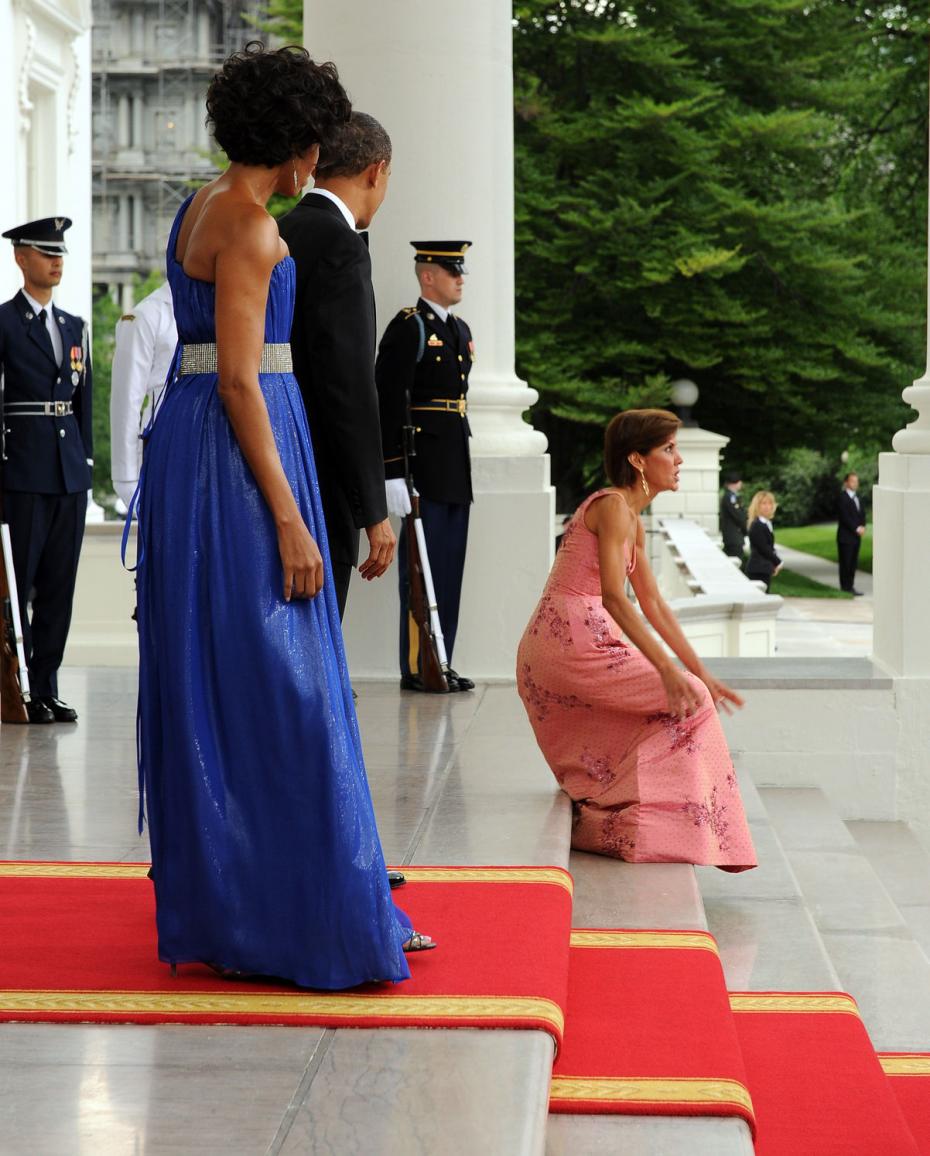 Senhora baixa, franzina,Chefe do Cerimonial da Casa Branca, usando vestido rosa longo, ao caminhar junto ao tapete vermelho, cai sentada na escadaria da Casa Branca, na frente de todos os fotógrafos do mundo todo, durante a recepção ao Presidente do México.
