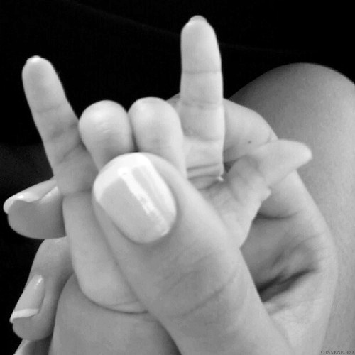 mão de mulher com unhas bem tratadas segurando a mão de um bebê recém nascido e com o dedão ela segura os dedilho anular e médio da criança formando o símbolo de heavy metal
