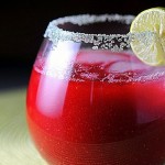 imagem de um copo baixo e arredondado, com suco de tomate e uma faixa cristais de sal na borda do copo que está enfeitado com uma rodela de limão