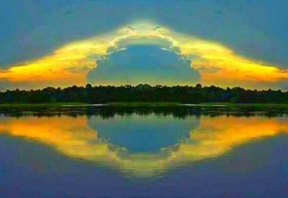 Imagem do Rio Amazonas, num entardecer, nuvens amarelas junto a mata em forma do losango da bandeira. A imagem está espelhada nas águas do rio. Exatamente a bandeira nacional.