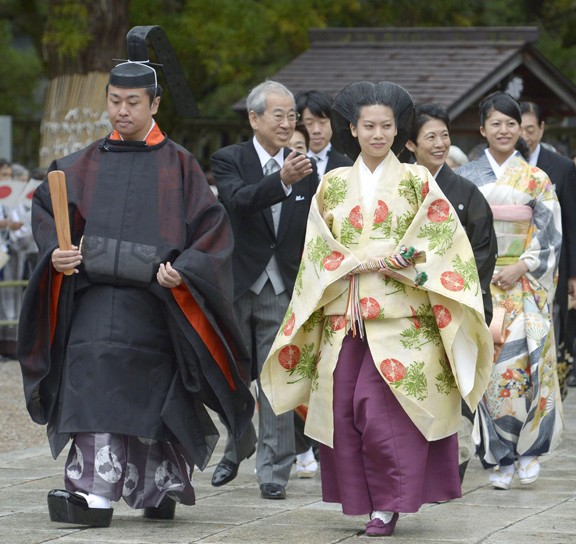 Princesa Noriko do Japão, e seu noivo, caminham um ao lado do outro, usando trajes típicos de um casamento shintoista, logo atrás um cortejo de inúmeras casais, os homens vestem fraque e as mulheres vestem trajes típicos japoneses.