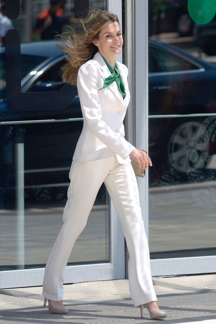 Rainha Letícia da Espanha, em foto de sua chegada a um evento, está andando elegantemente, usando um conjunto de alfaiataria e um lenço verde envolvendo o pescoço.