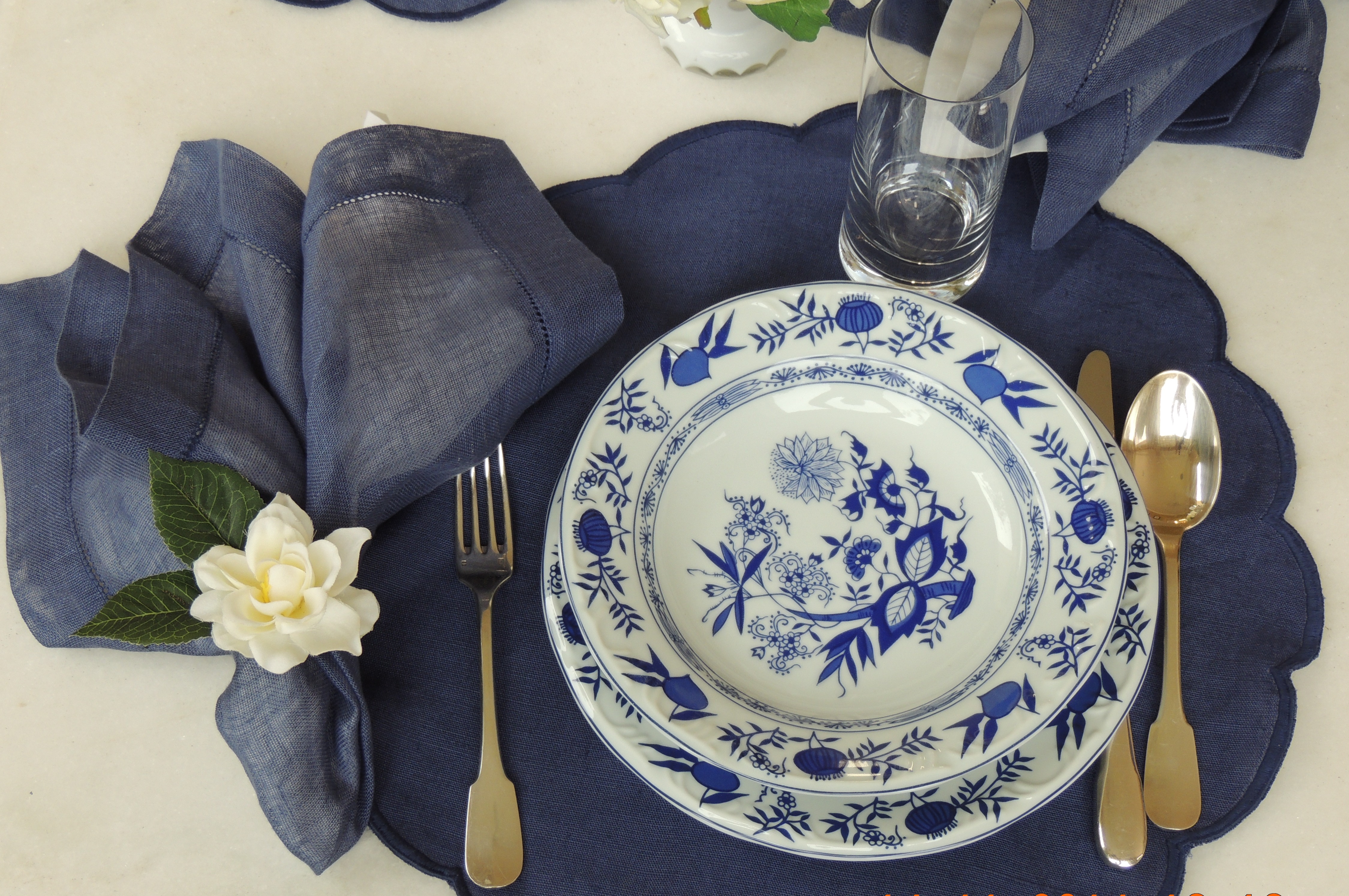Porcelanas Schmidt - Modelo Cebolinha, fundo branco com detalhes em azul, sobre a mesa com jogo americano azul, com talheres em prata, garfo a esquerda do prato.