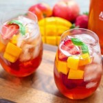 bandeja de madeira, com 2 copos estilo drink, com chá gelado, decorados com vários tipos de frutas cortadas em cubos, rodelas de limão e folhas de hortelã nas bordas