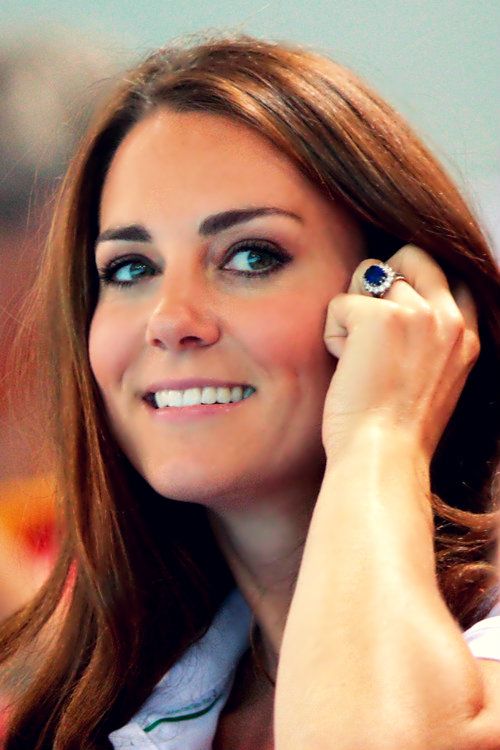 Princesa Kate Middleton, do Reino Unido, casada com Príncipe William, está sorrindo e tem a sua mão esquerda junto ao rosto mostrando seu lindo anel,