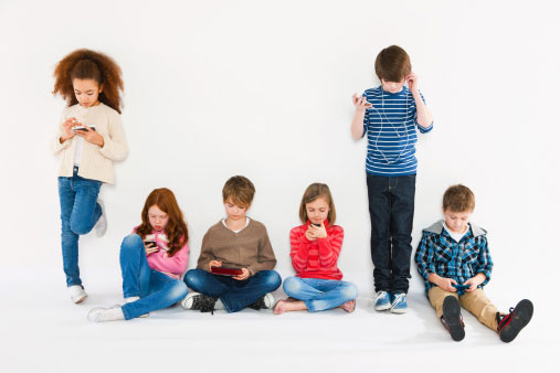 a foto mostra 6 crianças entre 8 e 10 anos com celular. duas estão em pé e as outras sentadas. Estão lado a lado e cada uma está com seu celular, algumas digitando e outras ouvindo música