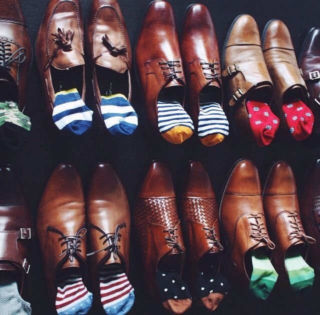 sapatos em tons marrons, tendo cada um com um tipo de meia colorida. algumas listradas em tons azuis, outras vermelhas, outra com bolinhas brancas no fundo azul.
