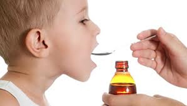 a foto mostra um menino loirinho de 5 anos de perfil, abrindo a boca para tomar remedio.