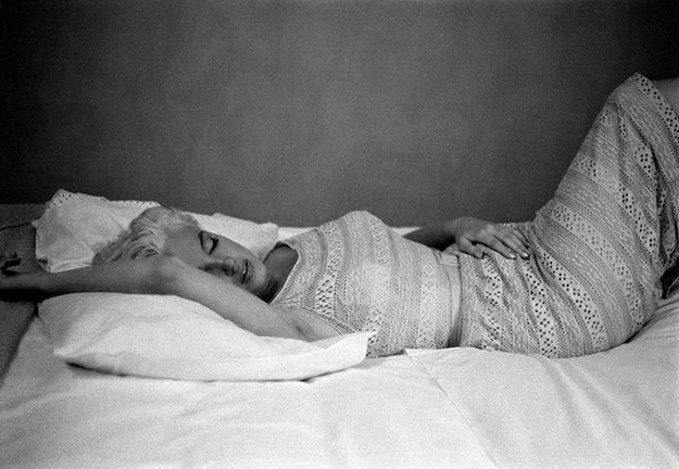 a atriz Marilyn Monroe está deitada em dormindo em uma foto em preto e branco com o braço direito sobre a cabeça em uma atitude de abandono e conforto.