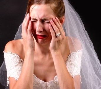 mulher usando vestido de noiva , com véu e grinalda, chora e está com as mãos no rosto em cena de desespero.