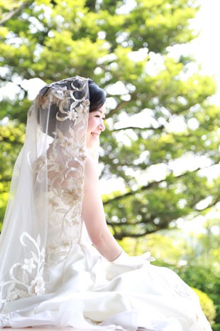 mulher japonesa, ela está sentada num jardim, usando vestido de noiva.