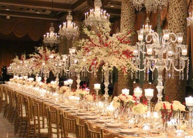 mesa de banquete, completa com porcelanas e prataria, ainda com vasos altos de flores e inúmeros castiçais complementam a decoração