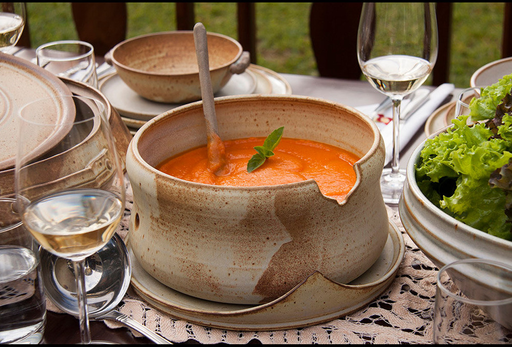 mesa de jantar, tendo ao centro uma sopeira em cerâmica, com creme de abóbora, outros detalhes decoração a mesa. verduras, taças.