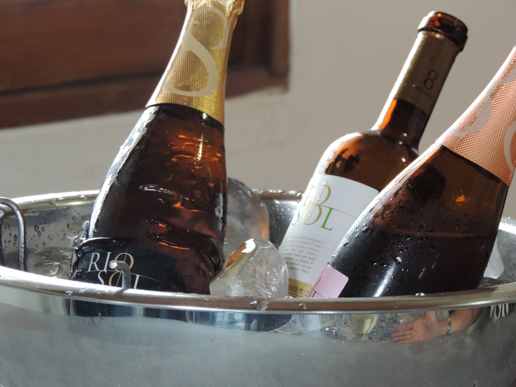 Num balde de gelo, tres garrafas de vinhos estão gelando, todas sem rolha, e o balde de prata.