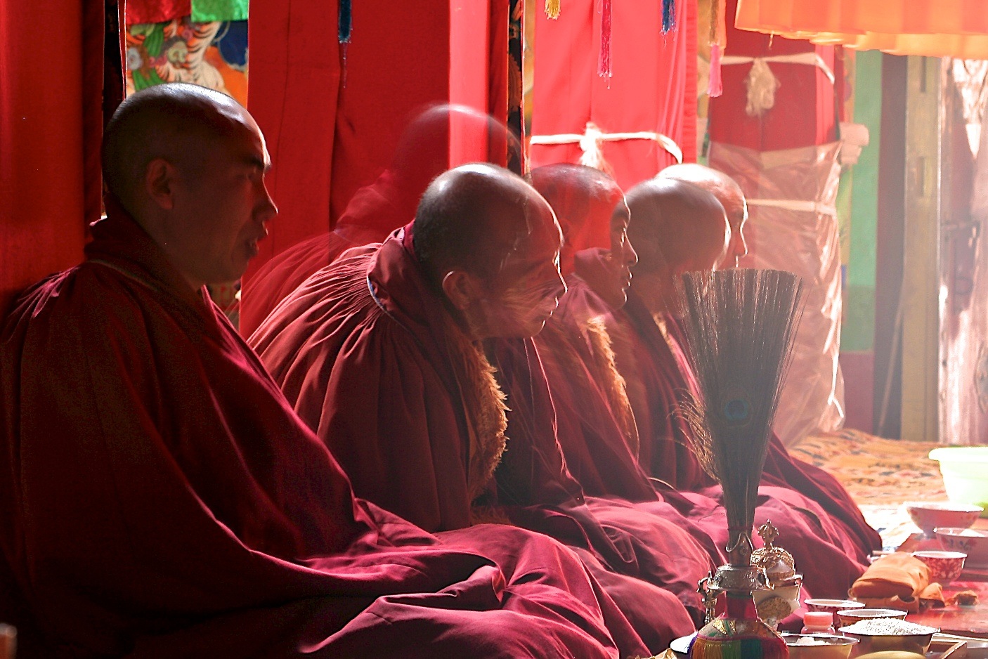 Num templo budista, cinco monges budistas tibetanos, conhecidos por suas carecas lisas, meditam usando seus mantos grenas, estão sentados com pernas cruzadas, um ao lado do outro, na posição tradicional budista,