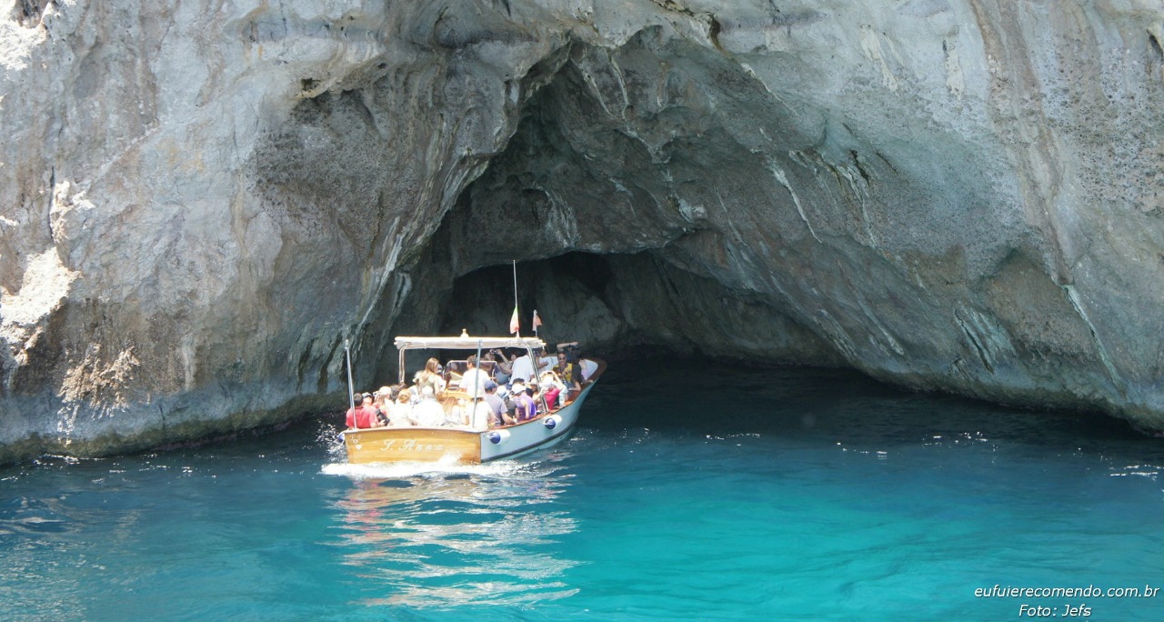 gruta de pedra no mar, com um barco com turistas, visitam esse ponto turístico de Capri, Italia. Um mar azul , águas límpidas e cor azul turquesa muito clara.