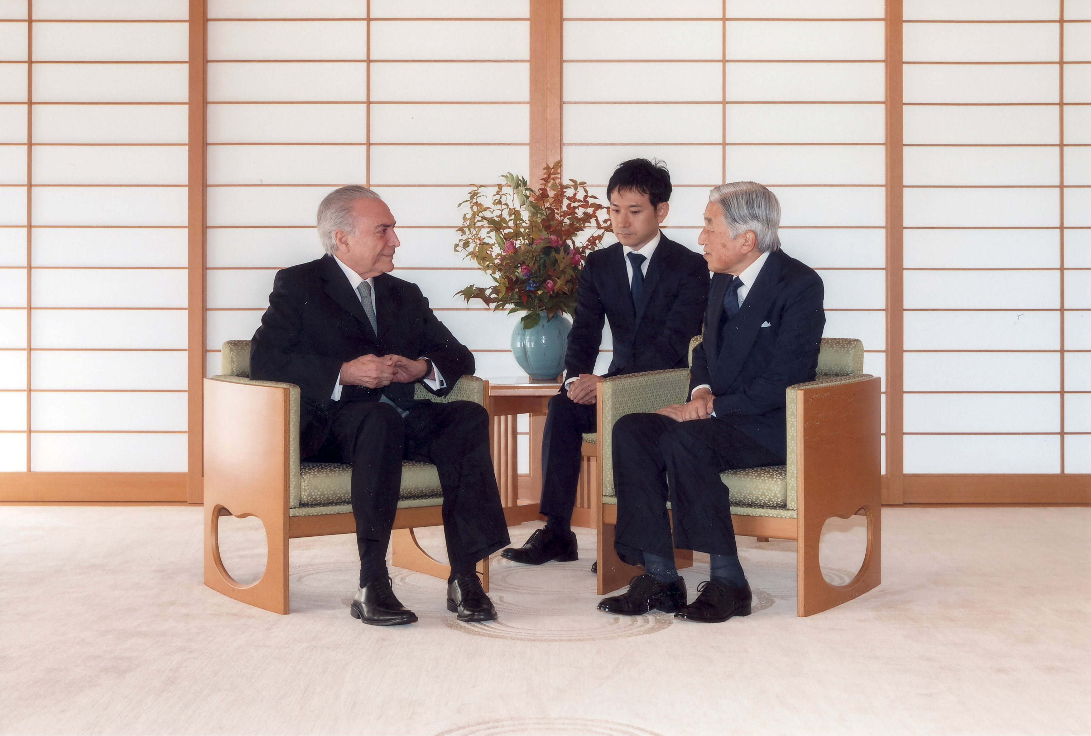 Sua Majestade Imperador Akihito do Japão recebe na Casa Imperial Japonesa o Presidente Michel Temer, do Brasil, estãn no Salão Imperial sentados o a ambos usam terno escuro , camisa branca e gravata escura. Estão conversando.