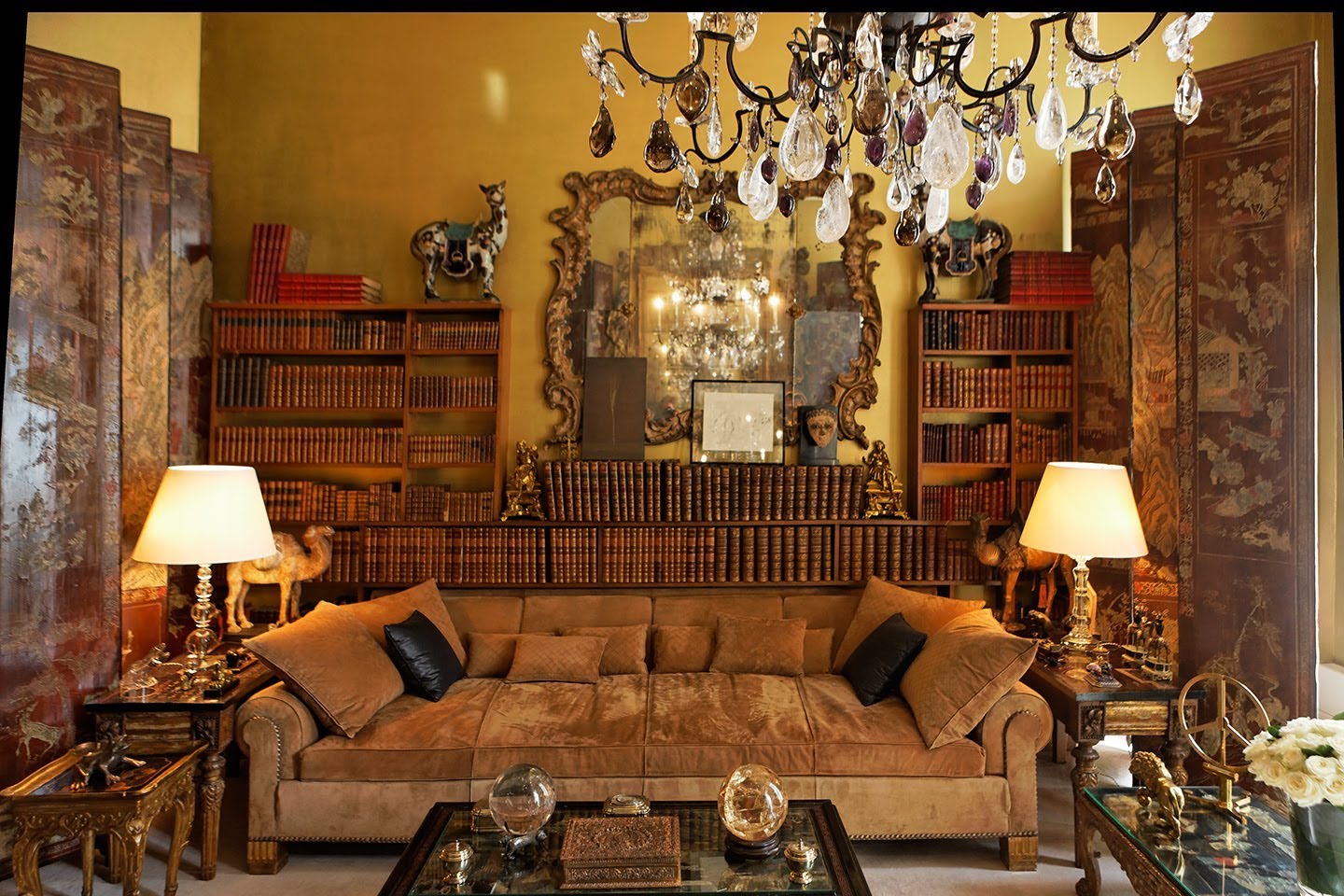Sala da casa-atelier da estilista Coco Chanel - tudo em pares - almofadas , cor preta - lustres , bolas de cristal, animais em artesanato- e ao fundo uma enorme biblioteca de livros