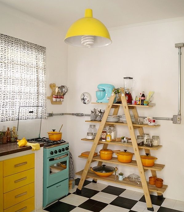 cozinha com piso preto e branco apresenta fogão azul claro e geleiro amarelo. Ao fundo a prateleira é uma escada de prateleiras onde os potes e objetos coloridos enfeitam o ambiente...