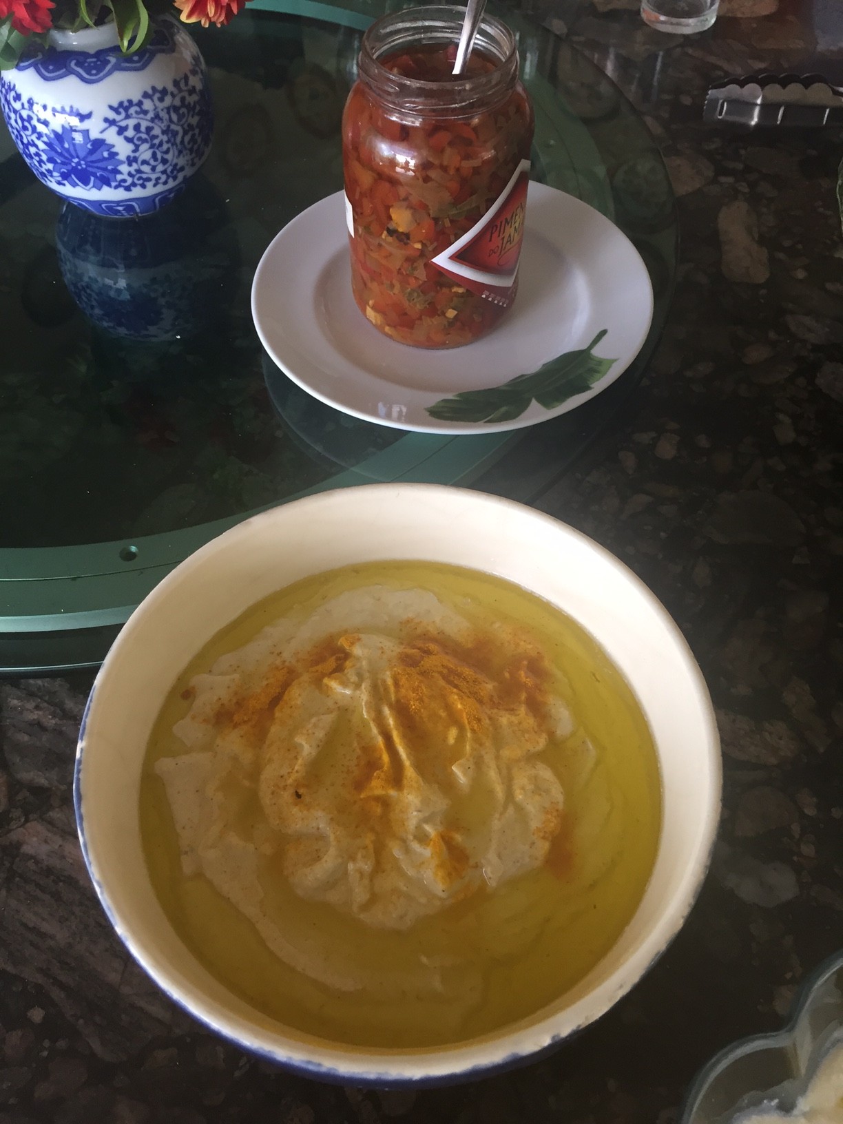 uma cumbuca mostra pasta de grão de bico salpicada de páprica vermelha e ao fundo um pote de pimenta vermelha no azeite