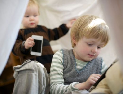 duas crianças uma mais velha do que a outra (5 anos) e (1 anos), que estão brincando um smartphones e tablets.